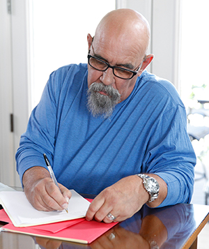 Hombre sentado a una mesa, escribiendo.